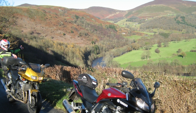 a large valley with trees and a river in the sun in north wales, 2 bikes in the foreground
